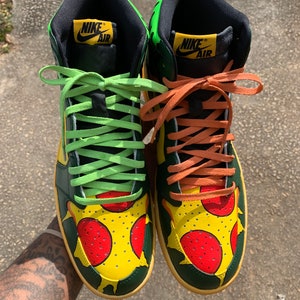 May include: Pair of high-top sneakers with a pizza-themed design. The shoes feature a yellow base with red pepperoni and green accents. The laces are lime green and orange. The Nike Air logo is visible on the tongue.