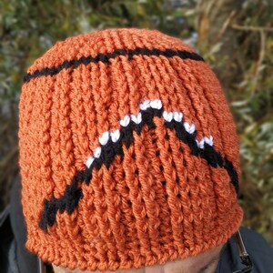 May include: A knitted orange beanie hat with a black and white basketball design.