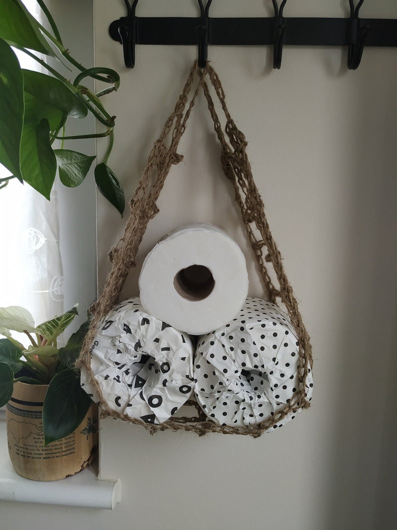 May include: Three rolls of toilet paper hanging from a macrame wall hanging. The rolls are white with black polka dots and one is plain white.