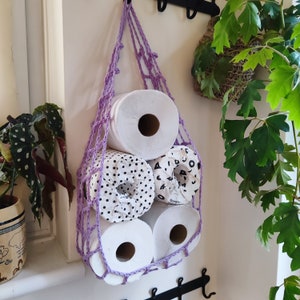 May include: Purple crocheted hanging storage with four rolls of toilet paper. Two rolls have black and white polka dots, one roll has a black and white geometric pattern, and one roll is plain white.