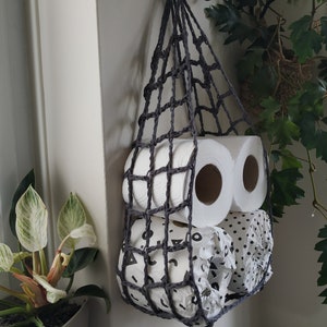 May include: A gray crocheted hanging storage organizer with two rolls of toilet paper and a third roll with a black and white polka dot pattern.