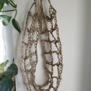 May include: A brown, crocheted, net-like bag hanging from a hook. The bag is made of natural fibers and has a loose, open weave.