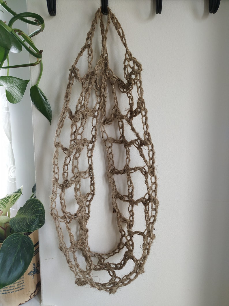 May include: A brown, crocheted, net-like bag hanging from a hook. The bag is made of natural fibers and has a loose, open weave.