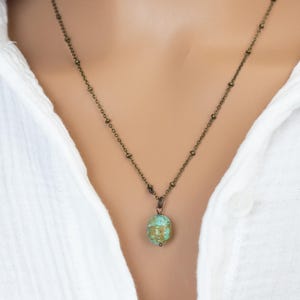 May include: A delicate bronze chain necklace with a turquoise and gold pendant. The pendant is a round, slightly irregular shape.