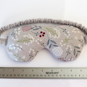 May include: A gray sleep mask with a floral pattern featuring white, pink, and red flowers. The mask has an elastic band for a comfortable fit.