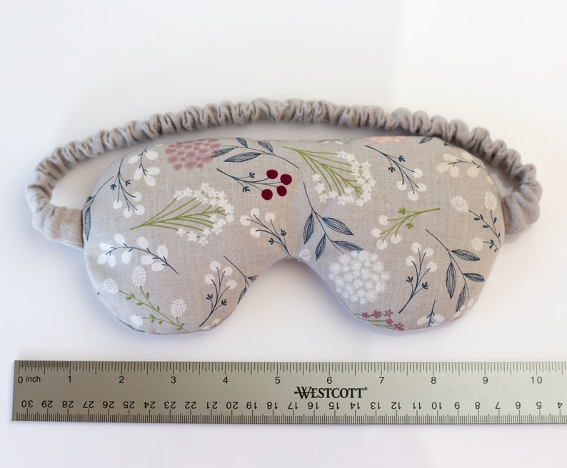 May include: A gray sleep mask with a floral pattern featuring white, pink, and red flowers. The mask has an elastic band for a comfortable fit.