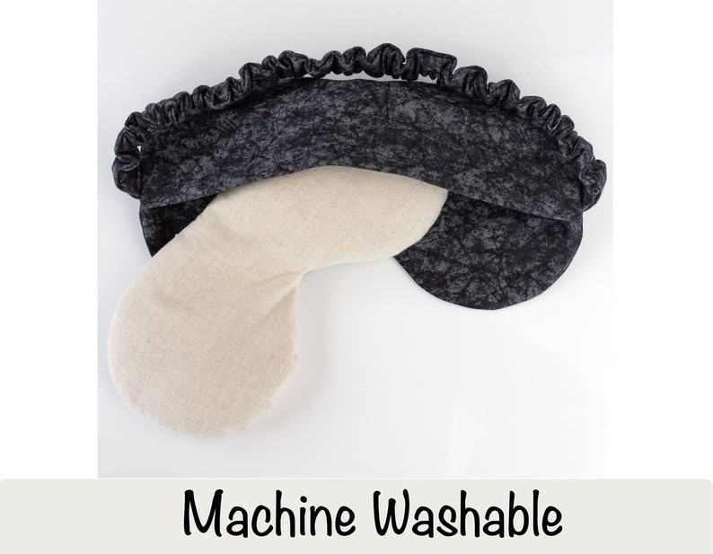 May include: A black and white eye mask with a white, u-shaped pillow inside. The eye mask is made of a soft, textured fabric and has a ruffled edge. The text "Machine Washable" is printed below the image.