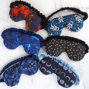 May include: Six different sleep masks with various space-themed patterns. The masks are made of soft fabric and have adjustable elastic straps. The patterns include stars, planets, astronauts, and galaxies.