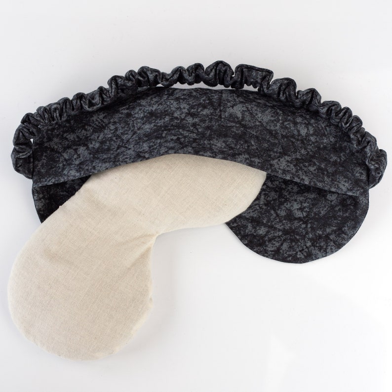 May include: A black and white eye mask with a soft, beige fabric lining. The eye mask is made of a soft, comfortable material and has a contoured shape to fit comfortably over the eyes.