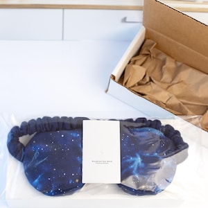 May include: A blue weighted eye mask with a galaxy print. The mask is packaged in a clear plastic bag with a white card that says "Weighted Eye Mask Instructions".