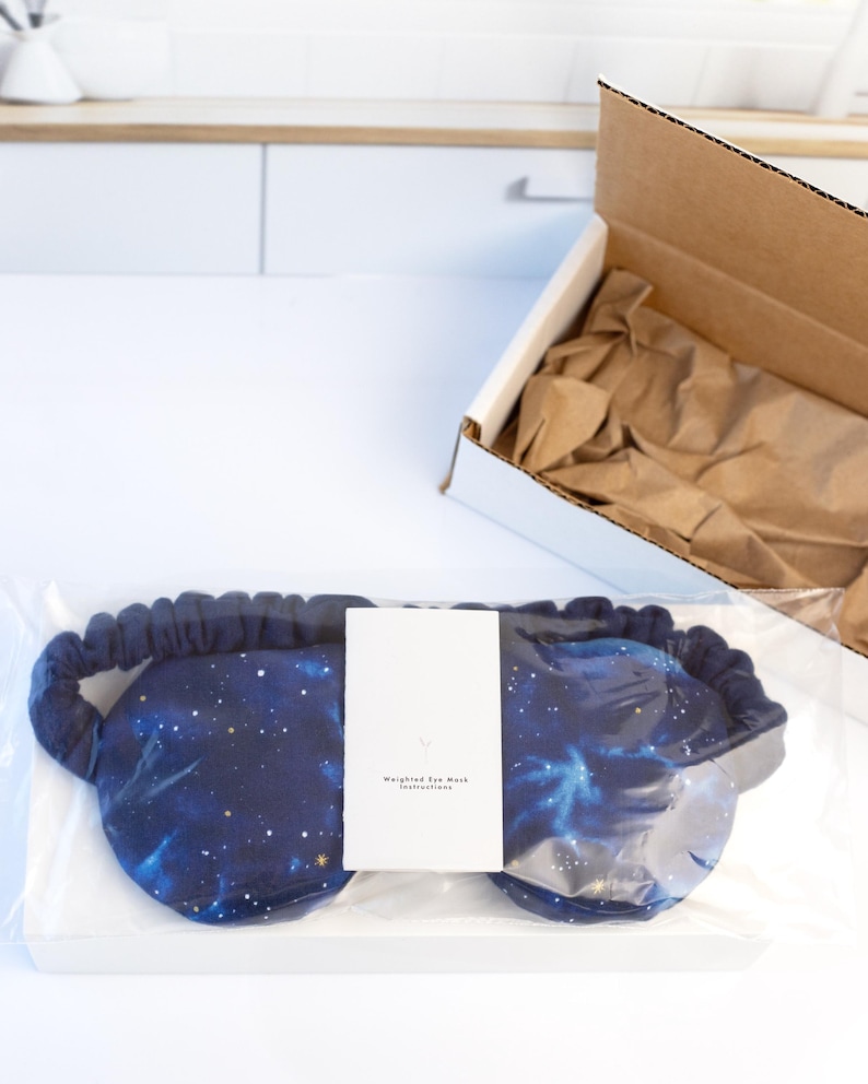 May include: A blue weighted eye mask with a galaxy print. The mask is packaged in a clear plastic bag with a white card that says "Weighted Eye Mask Instructions".