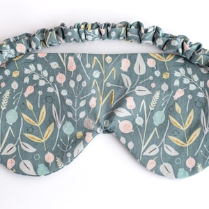 May include: A teal blue sleep mask with a floral pattern. The mask has an elastic band for a comfortable fit.