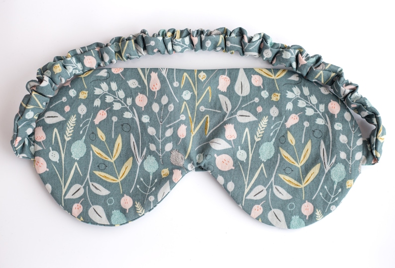 May include: A teal blue sleep mask with a floral pattern. The mask has an elastic band for a comfortable fit.