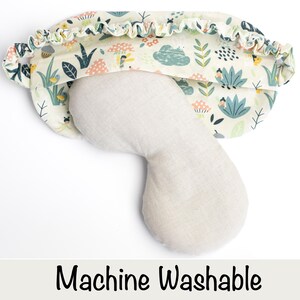 May include: A white sleep mask with a floral print and a light beige eye mask. The sleep mask has a ruffled edge and the text "Machine Washable" is printed below the image.
