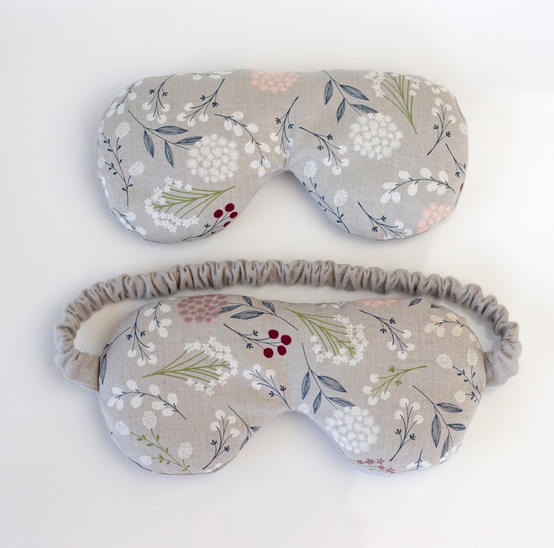 May include: Two gray eye masks with a floral pattern. The top mask is a simple eye mask, while the bottom mask has an elastic band.