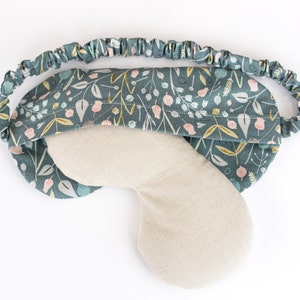 May include: A teal blue sleep mask with a floral pattern and a light beige fabric lining. The mask has an elastic band for a comfortable fit.