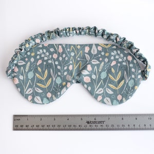 May include: A blue sleep mask with a floral pattern featuring pink, white, and yellow flowers. The mask has a gathered elastic band.