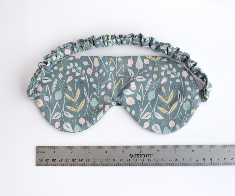 May include: A blue sleep mask with a floral pattern featuring pink, white, and yellow flowers. The mask has a gathered elastic band.