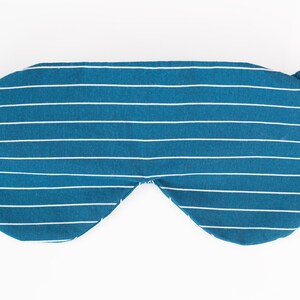 Puede incluir: Una m&aacute;scara para dormir a rayas blancas y azul verdoso con bandas el&aacute;sticas. La m&aacute;scara est&aacute; dise&ntilde;ada para bloquear la luz y promover la relajaci&oacute;n. La tela tiene un patr&oacute;n de rayas horizontales.