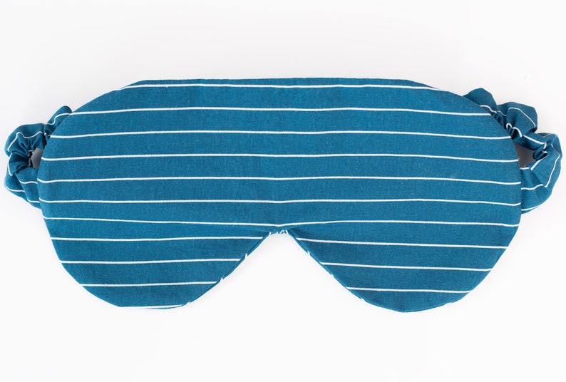 Puede incluir: Una m&aacute;scara para dormir a rayas blancas y azul verdoso con bandas el&aacute;sticas. La m&aacute;scara est&aacute; dise&ntilde;ada para bloquear la luz y promover la relajaci&oacute;n. La tela tiene un patr&oacute;n de rayas horizontales.