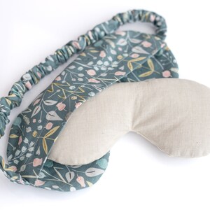 May include: A teal blue sleep mask with a floral pattern and a light beige fabric lining. The mask has an elastic band for a comfortable fit.