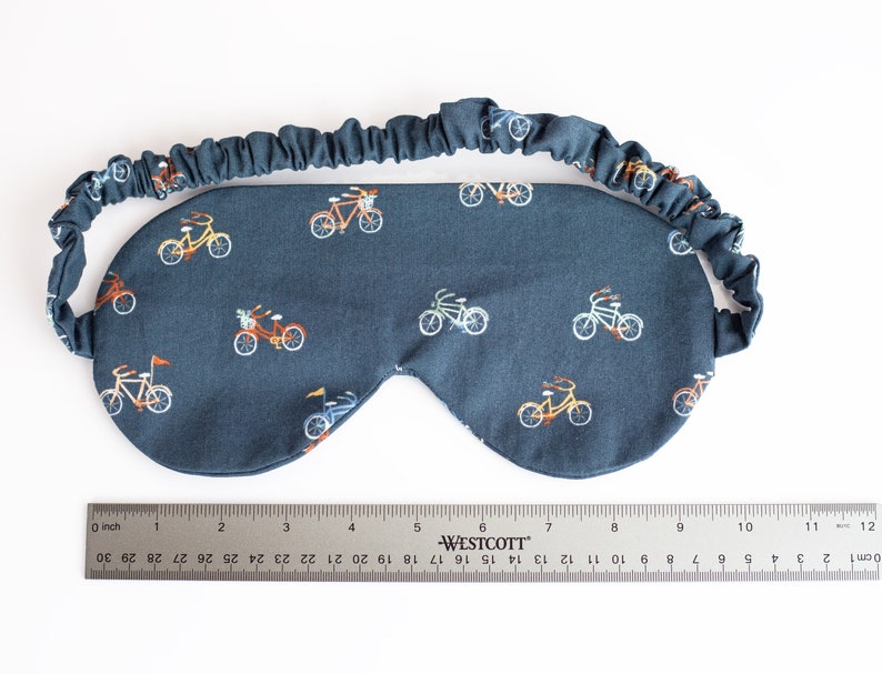 以下が含まれることがあります： 小さなカラフルな自転車が繰り返し描かれた、濃い青色のアイマスク。快適なフィット感を実現する伸縮性のあるバンドが付いています。