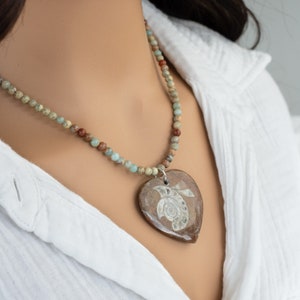 May include: A heart-shaped pendant necklace with a fossilized ammonite design. The necklace is made with a light green and brown speckled stone.