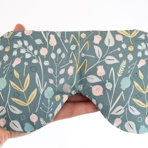May include: A teal blue sleep mask with a floral pattern featuring pink, white, and gold flowers and leaves.