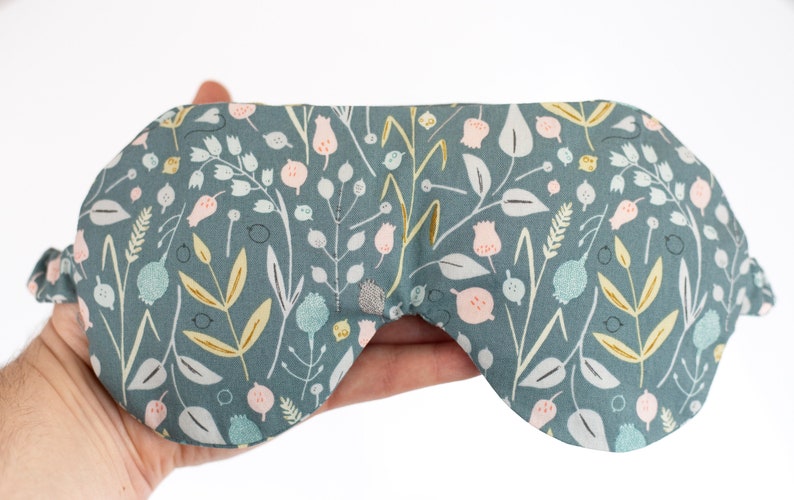 May include: A teal blue sleep mask with a floral pattern featuring pink, white, and gold flowers and leaves.