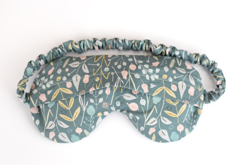 May include: A blue sleep mask with a floral pattern. The mask has an elastic band for a comfortable fit.