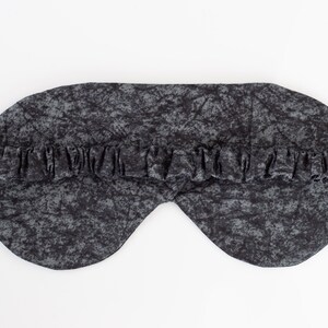 May include: A black sleep mask with a gray and black marbled pattern. The mask has an elastic band for a comfortable fit.