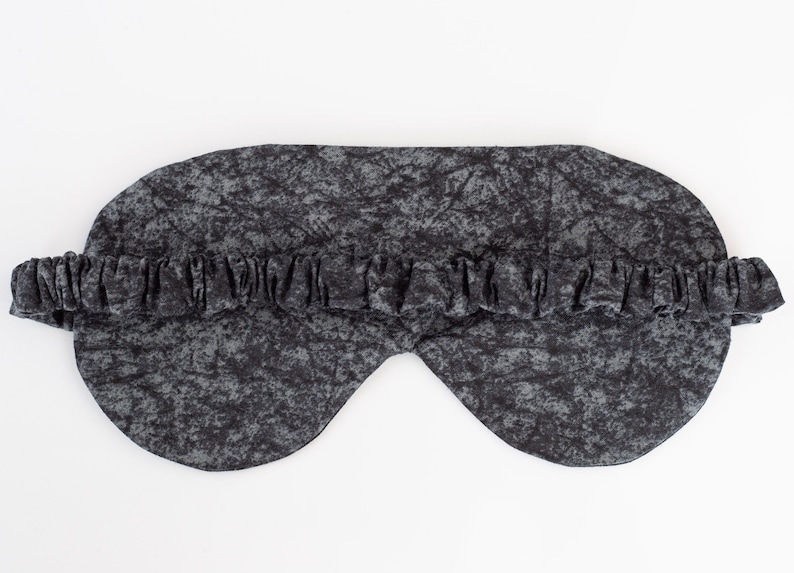 May include: A black sleep mask with a gray and black marbled pattern. The mask has an elastic band for a comfortable fit.