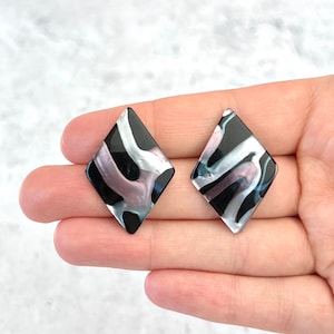 May include: A pair of black and white diamond-shaped earrings with a swirling pattern. The earrings have a pearlescent finish.