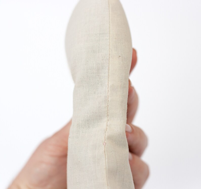 May include: A close-up of a cream-colored fabric pouch with a seam down the center. The pouch is held in a hand.