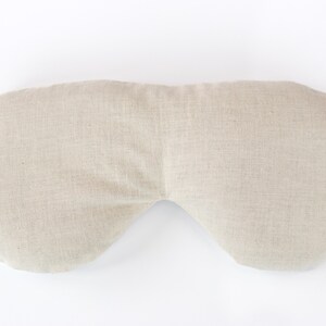 May include: A beige linen eye pillow, shaped like a crescent moon, for relaxation and sleep.