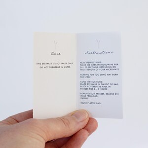 May include: Instructions for using a reusable eye mask. The card is white with black text and a small symbol at the top. The text reads: "Care: This eye mask is spot wash only. Do not submerge in water." and "Instructions: Heat Instructions: Place eye mask in microwave for 50-70 seconds, depending on the strength of your microwave. Heating for too long may burn the strap. Cool Instructions: Place eye mask in plastic zip bag. Place covered eye mask in freezer for 2-3 hours. Remove from freezer, remove eye mask from bag. Enjoy! Reuse plastic bag."