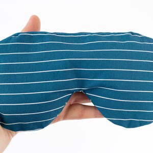 Puede incluir: M&aacute;scara para dormir a rayas blancas y azul verdoso. La m&aacute;scara est&aacute; hecha de tela y tiene un patr&oacute;n de rayas horizontales. La m&aacute;scara tiene una forma curva para adaptarse a los ojos y tiene correas de tela a cada lado.
