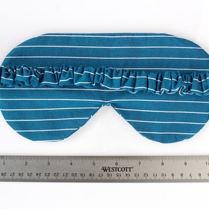 Puede incluir: M&aacute;scara para dormir a rayas blancas y azul verdoso con una banda el&aacute;stica con volantes. La m&aacute;scara mide aproximadamente 20 cm de largo, con una regla en la imagen para la escala. La m&aacute;scara est&aacute; dise&ntilde;ada para bloquear la luz.