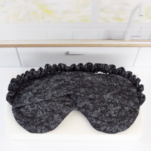 May include: A black sleep mask with a gray and black marbled pattern. The mask has a ruffled edge.