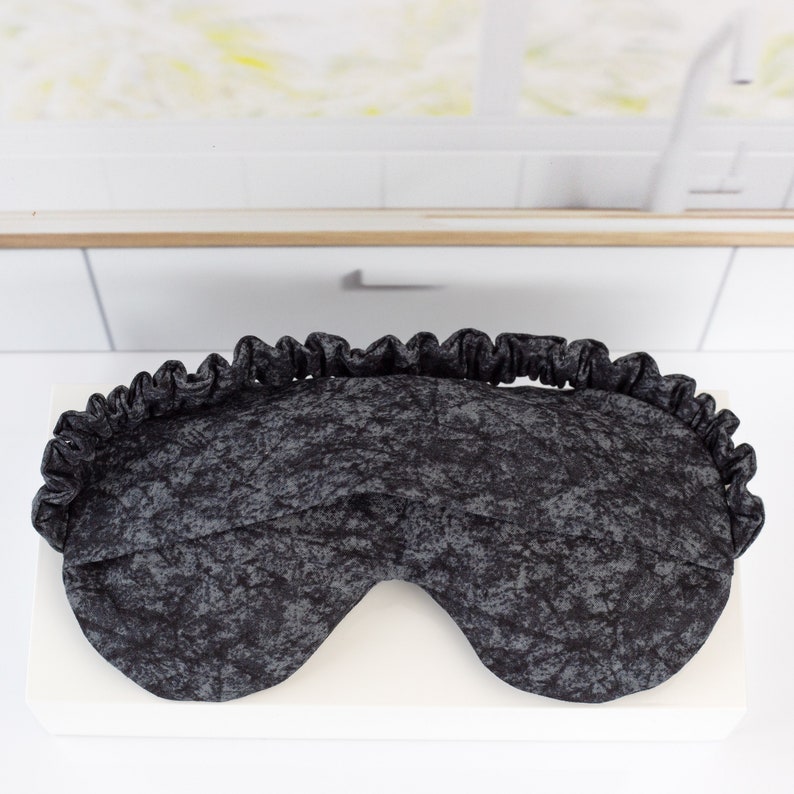 May include: A black sleep mask with a gray and black marbled pattern. The mask has a ruffled edge.
