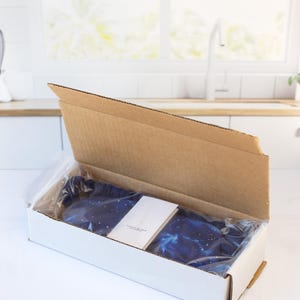 May include: A blue sleep mask with a galaxy print inside a white cardboard box. The box is open and the sleep mask is visible.