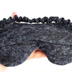 May include: A black sleep mask with a gray and black marbled pattern. The mask has an elastic band for a comfortable fit.