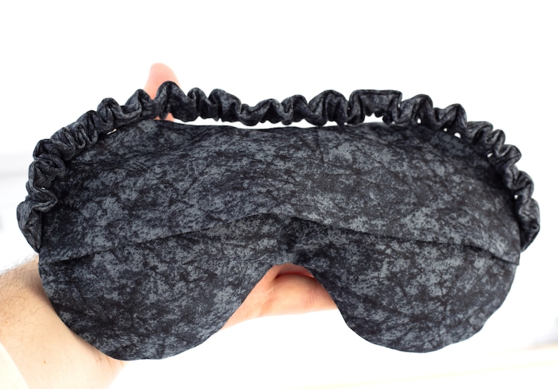 May include: A black sleep mask with a gray and black marbled pattern. The mask has an elastic band for a comfortable fit.