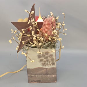 May include: A rustic, decorative box with a brown star, fabric pumpkins, and berry sprigs. The box features a landscape scene and a warm, glowing light. The design has a country or farmhouse aesthetic.