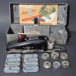 May include: A vintage White Magic Key buttonholer kit in a gray case. The kit includes a black buttonholer machine, bobbins, and buttonhole templates. The case has a printed instruction sheet with the text "White Magic Key Buttonholer".
