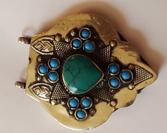 May include: A gold-toned pendant with a turquoise stone in the center and blue stones surrounding it. The pendant has intricate details and a decorative design.