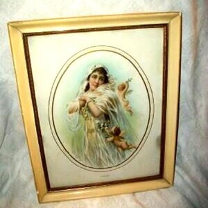 May include: A framed vintage print featuring a woman in a flowing white gown and veil, holding a small cherub. The artwork is set within an oval frame, surrounded by a cream-colored border and a gold-toned wooden frame.
