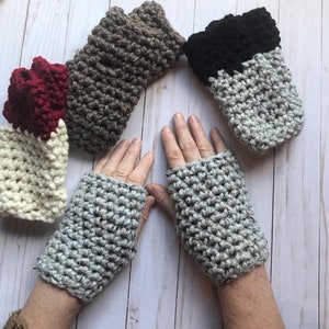 May include: Five pairs of crocheted fingerless gloves in various colors, including gray, brown, black, white, and red. The gloves are made with a textured stitch and are shown on a wooden surface.