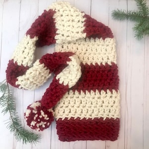 May include: A crocheted hat and scarf set in red and white stripes. The hat has a pompom on top and the scarf is long enough to wrap around the neck.