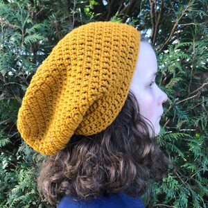May include: A mustard yellow crocheted beanie hat. The hat is slouchy and has a loose fit.